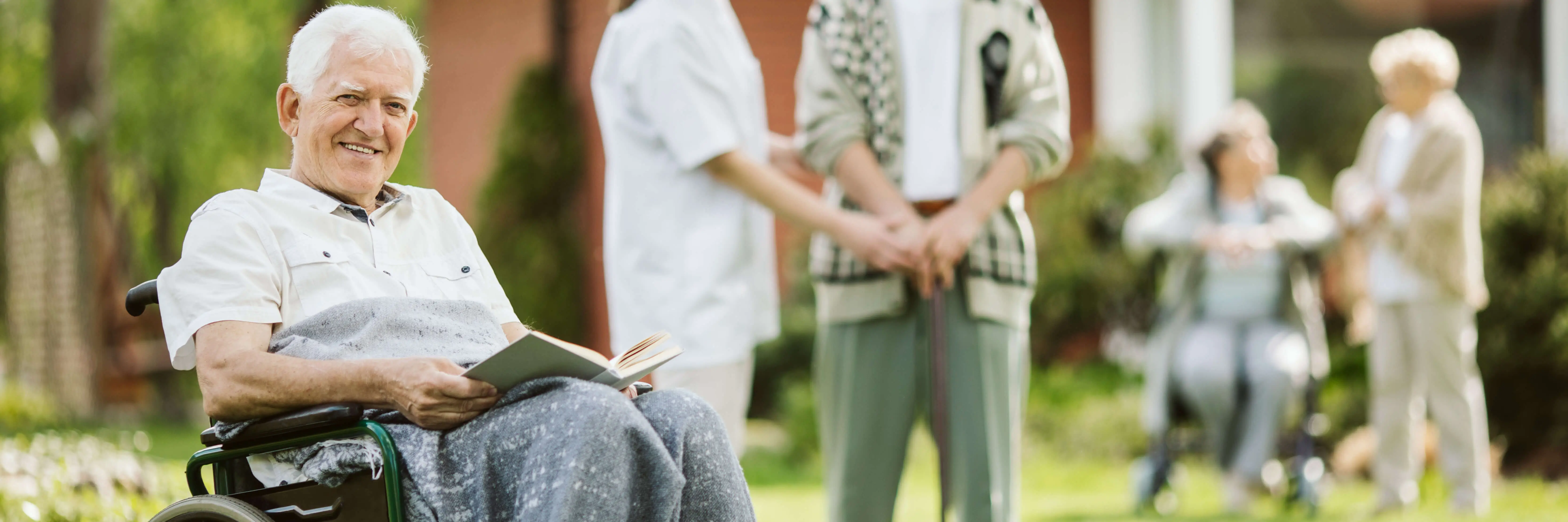 Elderly man smiling in a wheelchair while reading outdoors at a licensed OC HomeCare residential care home in Cypress, California, offering 24/7 senior living and dementia support
