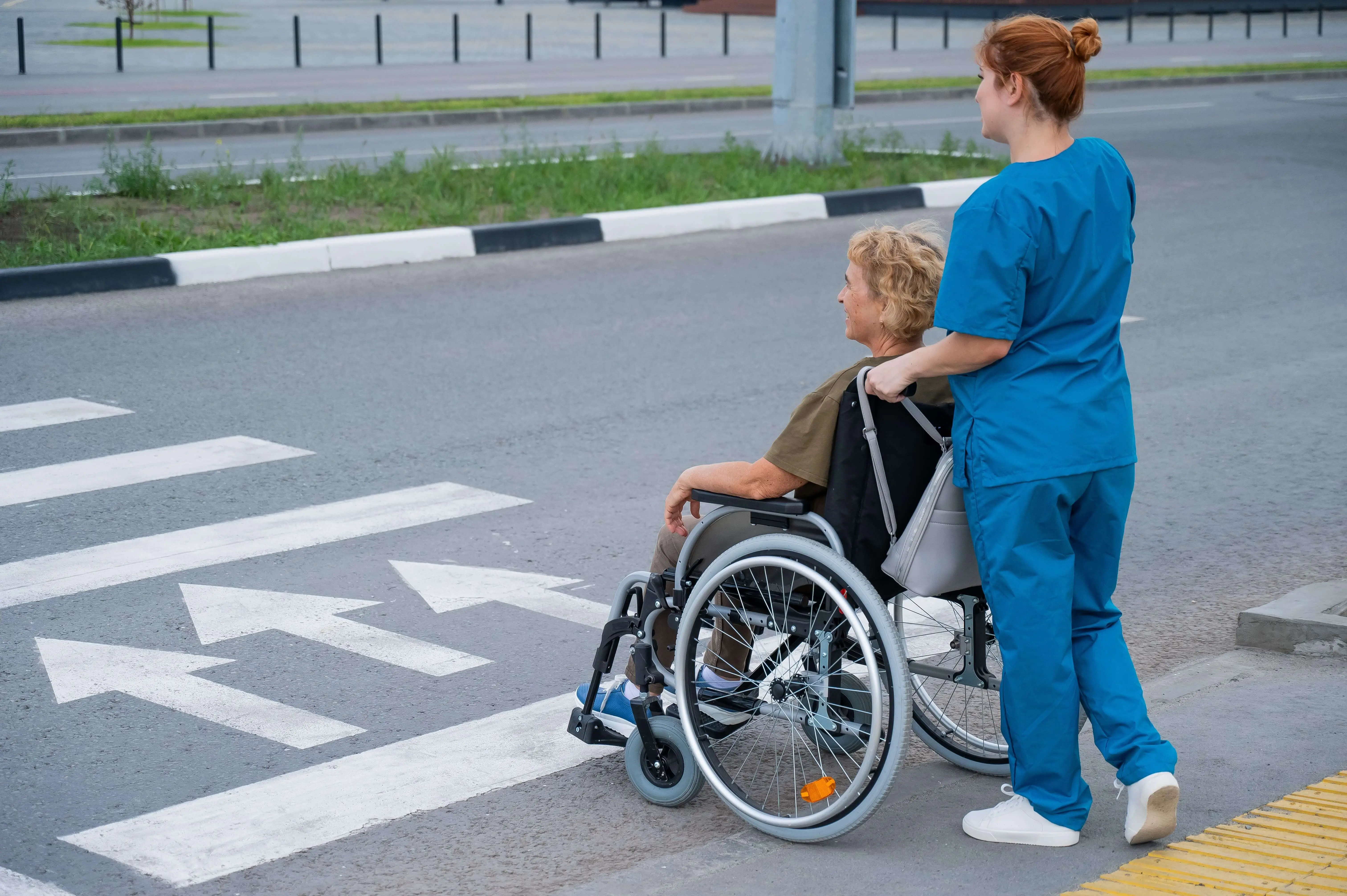 OC HomeCare caregiver assisting senior woman in wheelchair across crosswalk during non-emergency medical transportation in Orange County, CA